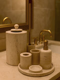 Luxury beige travertine marble bathroom accessory set displayed on a light stone countertop, featuring lotion dispenser, cotton jar, toothbrush holder, soap dish, tray, waste basket, and toilet brush — handcrafted Turkish travertine décor by Creative Home Designs.BAS-KRYKK-TRVTN-Go-S7,BAS-KRYKK-TRVTN-Go-S5