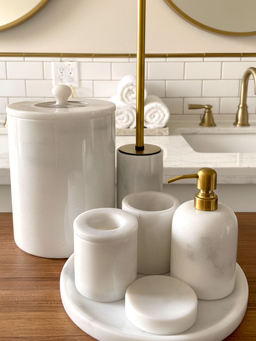 Luxury pearl white Afyon marble bathroom accessory set with gold accents displayed on a black marble countertop, featuring lotion dispenser, cotton box, toothbrush holder, soap dish, tray, waste basket, and toilet brush — handcrafted Turkish marble décor by Creative Home Designs,BAS-KRYKK-AFYON-PEARLGo-S7,BAS-KRYKK-AFYON-PEARLGo-S5