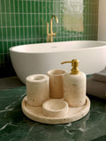 Luxury beige travertine marble bathroom accessory set displayed on a light stone countertop, featuring lotion dispenser, cotton jar, toothbrush holder, soap dish, tray, waste basket, and toilet brush — handcrafted Turkish travertine décor by Creative Home Designs.BAS-KRYKK-TRVTN-Go-S7,BAS-KRYKK-TRVTN-Go-S5