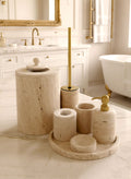 Luxury beige travertine marble bathroom accessory set displayed on a light stone countertop, featuring lotion dispenser, cotton jar, toothbrush holder, soap dish, tray, waste basket, and toilet brush — handcrafted Turkish travertine décor by Creative Home Designs.BAS-KRYKK-TRVTN-Go-S7,BAS-KRYKK-TRVTN-Go-S5