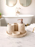 Luxury beige travertine marble bathroom accessory set displayed on a light stone countertop, featuring lotion dispenser, cotton jar, toothbrush holder, soap dish, tray, waste basket, and toilet brush — handcrafted Turkish travertine décor by Creative Home Designs.BAS-KRYKK-TRVTN-Cop-S7,BAS-KRYKK-TRVTN-Cop-S5