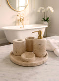 Luxury beige travertine marble bathroom accessory set displayed on a light stone countertop, featuring lotion dispenser, cotton jar, toothbrush holder, soap dish, tray, waste basket, and toilet brush — handcrafted Turkish travertine décor by Creative Home Designs.BAS-KRYKK-TRVTN-Go-S7,BAS-KRYKK-TRVTN-Go-S5