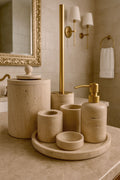 Luxury beige travertine marble bathroom accessory set displayed on a light stone countertop, featuring lotion dispenser, cotton jar, toothbrush holder, soap dish, tray, waste basket, and toilet brush — handcrafted Turkish travertine décor by Creative Home Designs.BAS-KRYKK-TRVTN-Go-S7,BAS-KRYKK-TRVTN-Go-S5