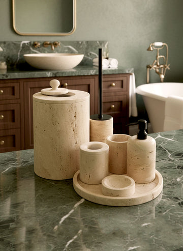 Luxury beige travertine marble bathroom accessory set displayed on a light stone countertop, featuring lotion dispenser, cotton jar, toothbrush holder, soap dish, tray, waste basket, and toilet brush — handcrafted Turkish travertine décor by Creative Home Designs.BAS-KRYKK-TRVTN-Bla-S7,BAS-KRYKK-TRVTN-Bla-S5