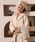 Woman wearing a beige Bamboo bathrobe by Creative Home, Gelin SPA Set with embroidery lace BRW-CH-GLNBei-Go-S-BO,BRW-CH-GLNBei-Go-S-BS,BRW-CH-GLNBei-Go-S-BST,BRW-CH-GLNBei-Go-M-BO,BRW-CH-GLNBei-Go-M-BS,BRW-CH-GLNBei-Go-M-BST,BRW-CH-GLNBei-Go-L-BO,BRW-CH-GLNBei-Go-L-BS,BRW-CH-GLNBei-Go-L-BST,BRW-CH-GLNBei-Go-XL-BO,BRW-CH-GLNBei-Go-XXL-BO,BRW-CH-GLNBei-Go-XXXL-BO,BRW-CH-GLNBei-Go-XL-BS,BRW-CH-GLNBei-Go-XXL-BS,BRW-CH-GLNBei-Go-XXXL-BS,BRW-CH-GLNBei-Go-XL-BST,BRW-CH-GLNBei-Go-XXL-BST,BRW-CH-GLNBei-Go-XXXL-BST